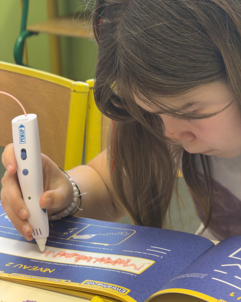 Gros plan sur un stylo 3D qui trace un trait de filament dans un livret